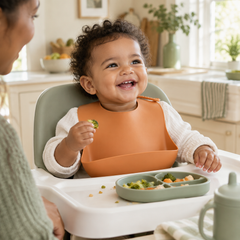 Baby wearing an orange silicone bib with a front catch pocket during mealtime